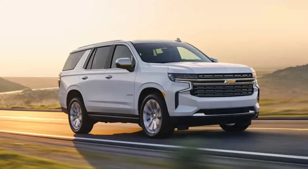 A white 2021 Chevy Tahoe is driving out of a corner past hills at sunset.