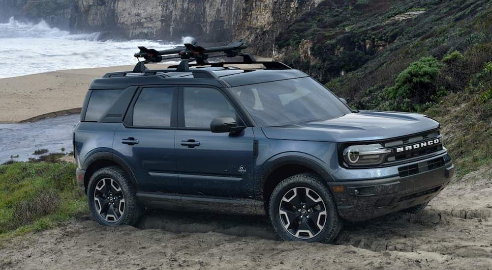 A dark blue 2021 Ford Bronco Sport is parked in the sand in front of the ocean and cliffs.