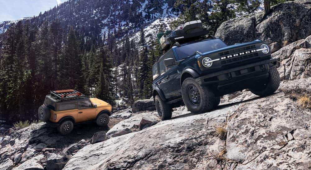 An orange 2021 Ford Bronco two-door is following a blue four-door up a rocky, mountain trail.