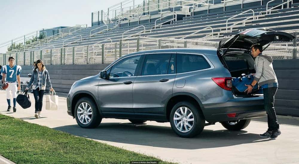 A man is loading gear into a grey 2021 Honda Pilot on a football field next to a woman and son who is in football uniform.