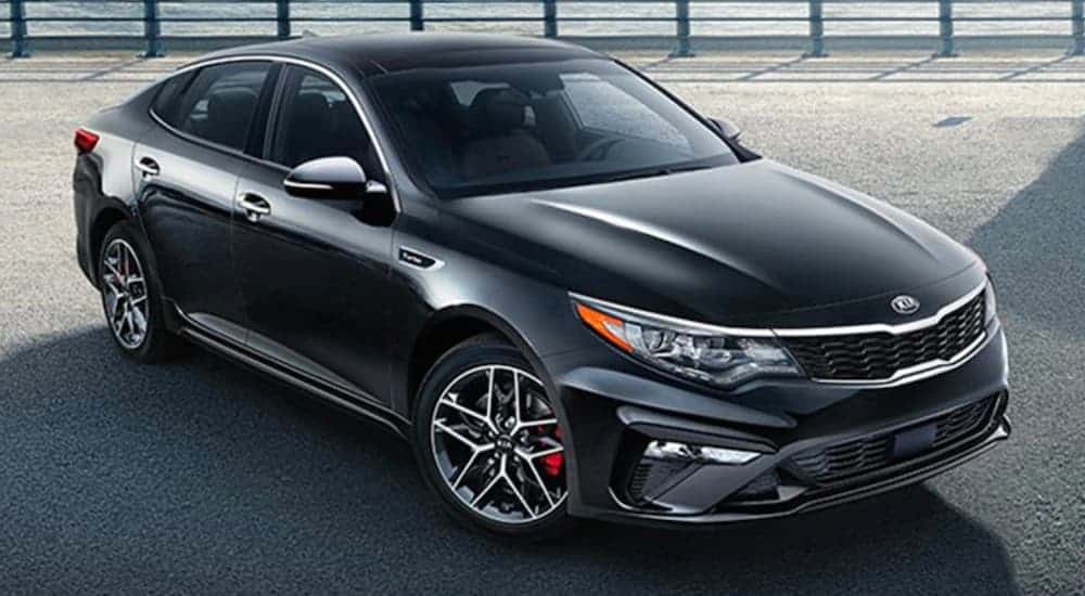 A black 2020 Kia Optima is parked in front of a pier.