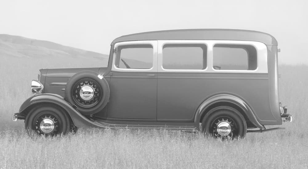 One of the original Chevy SUV models, a 1925 Chevy Suburban, is parked in a field and shown in black and white.