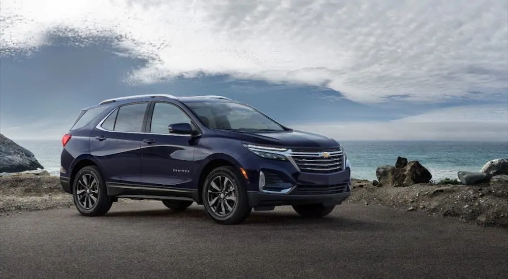 A new Chevy SUV model, a dark blue 2021 Chevy Equinox, is parked against a blue and cloudy sky.