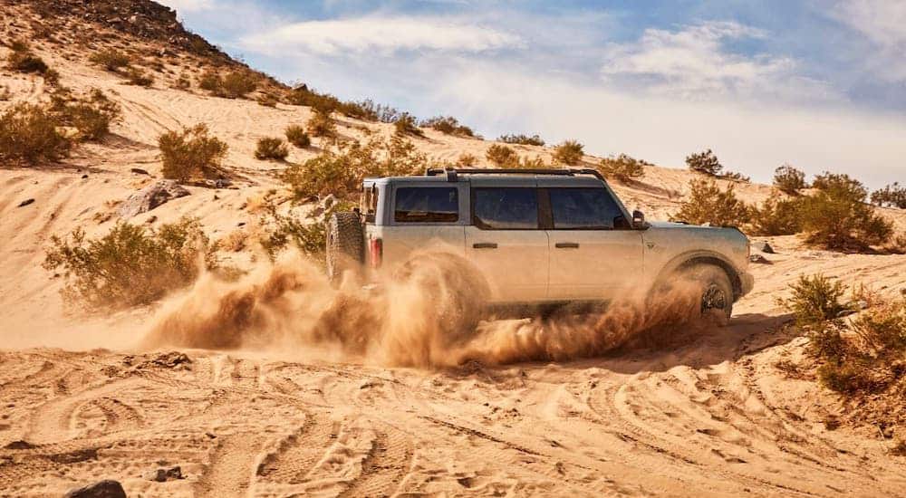 A silver 2021 Ford Bronco 4-door, that's coming to a Ford dealership near you, is driving in sand.
