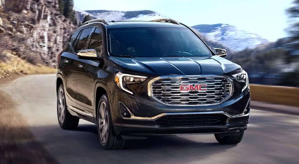 A black 2020 GMC Terrain is driving past mountains.