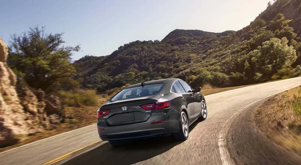 A grey 2021 Honda Insight is driving on a corner with mountains in the distance.