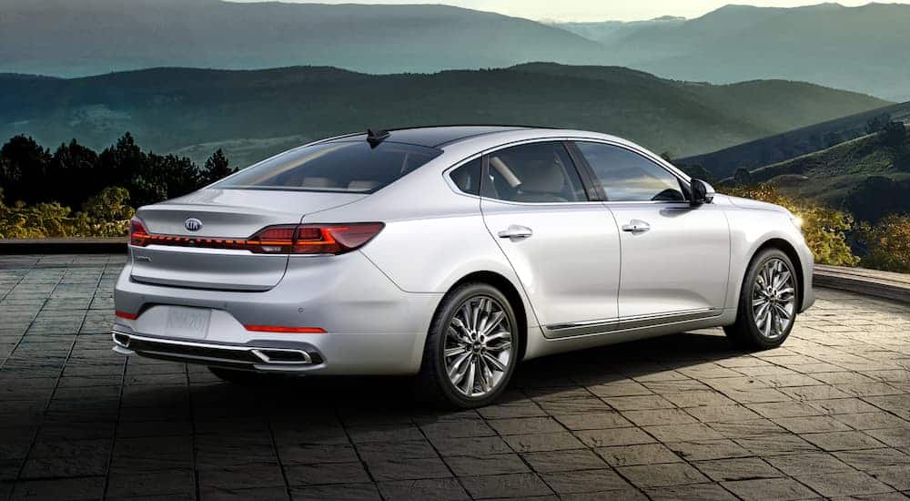 A silver 2020 Kia Cadenza is parked on pavers in front of dark mountains.