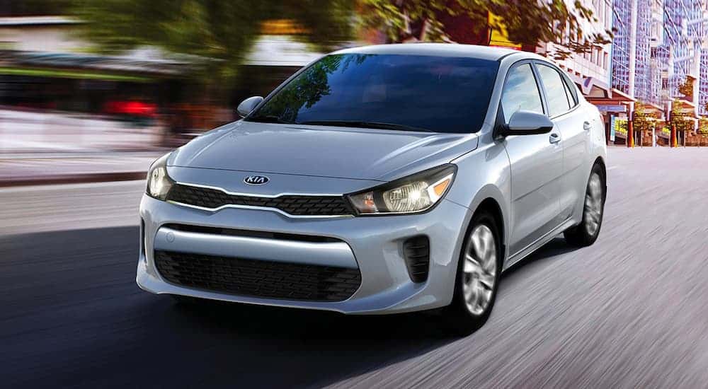 A grey 2020 Kia Rio is driving on a city street after leaving a Kia dealership.