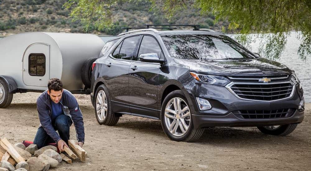 A dark grey 2020 Chevy Equinox is at a campsite with a tear drop camper as a man lights a fire.