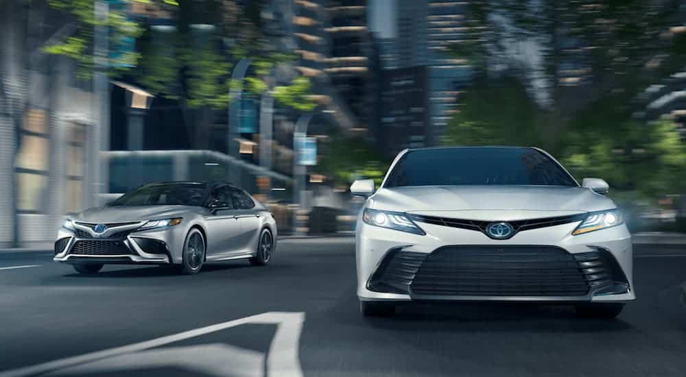 A silver and a white 2021 Toyota Camry are driving on a city street at night.