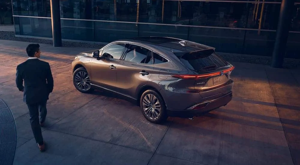 A man in a suit is walking past a grey 2021 Toyota Venza at a Toyota dealer at sunset.