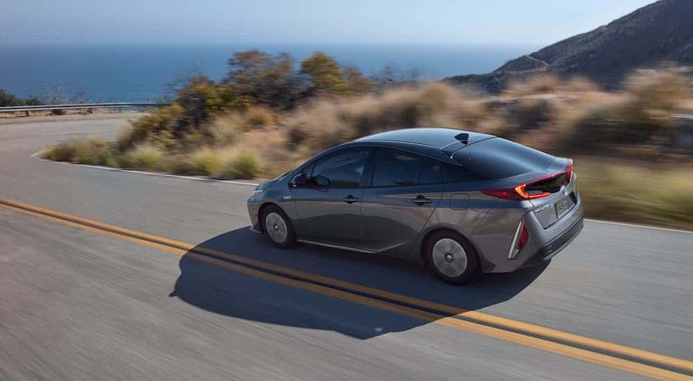 A grey 2020 Toyota Prius Prime is driving toward a sharp corner next to the ocean after leaving a Toyota dealer near me.