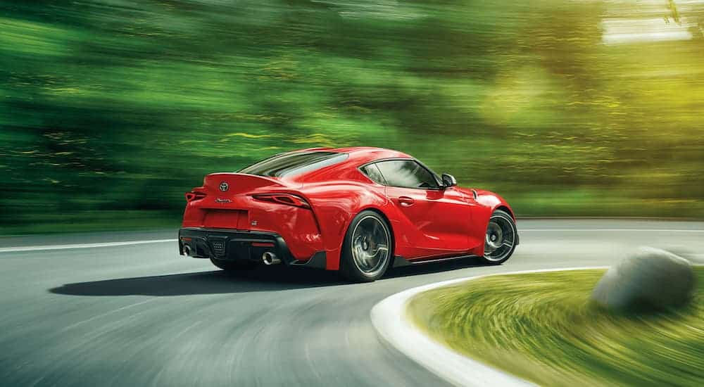 A red 2021 Toyota Supra is taking a corner on a racetrack past blurred trees.