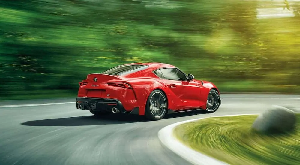 A red 2021 Toyota Supra is taking a corner on a racetrack past blurred trees.