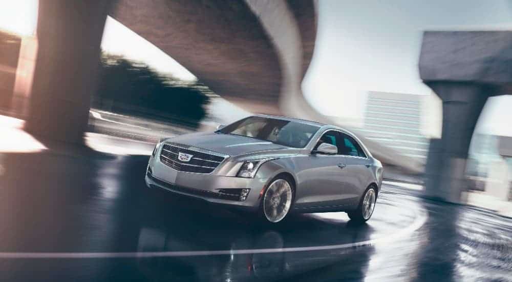 A silver 2018 Cadillac ATS is driving under a highway overpass.