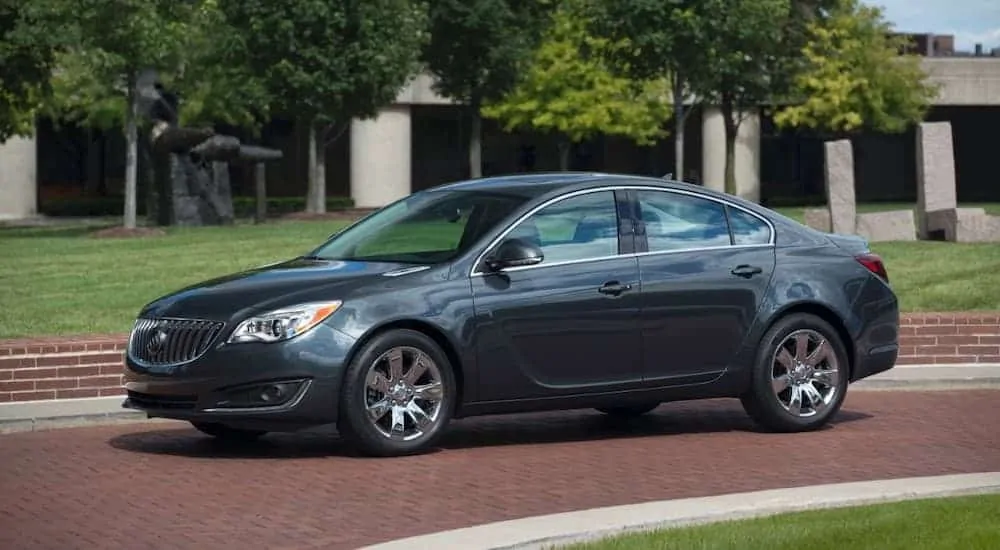 A dark grey 2016 Buick Regal is parked on bricks in front of a building.