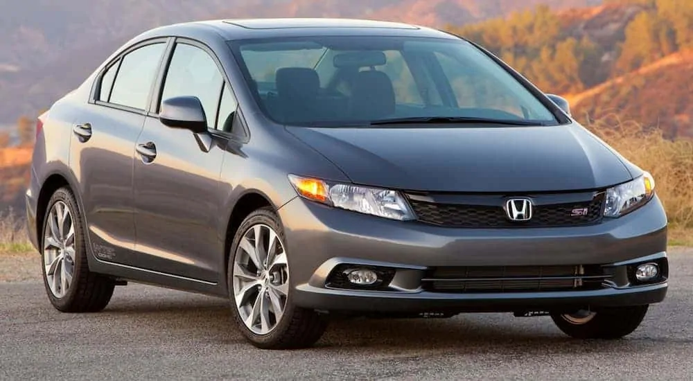 A grey 2012 Honda Civic is parked in front of fall foliage.