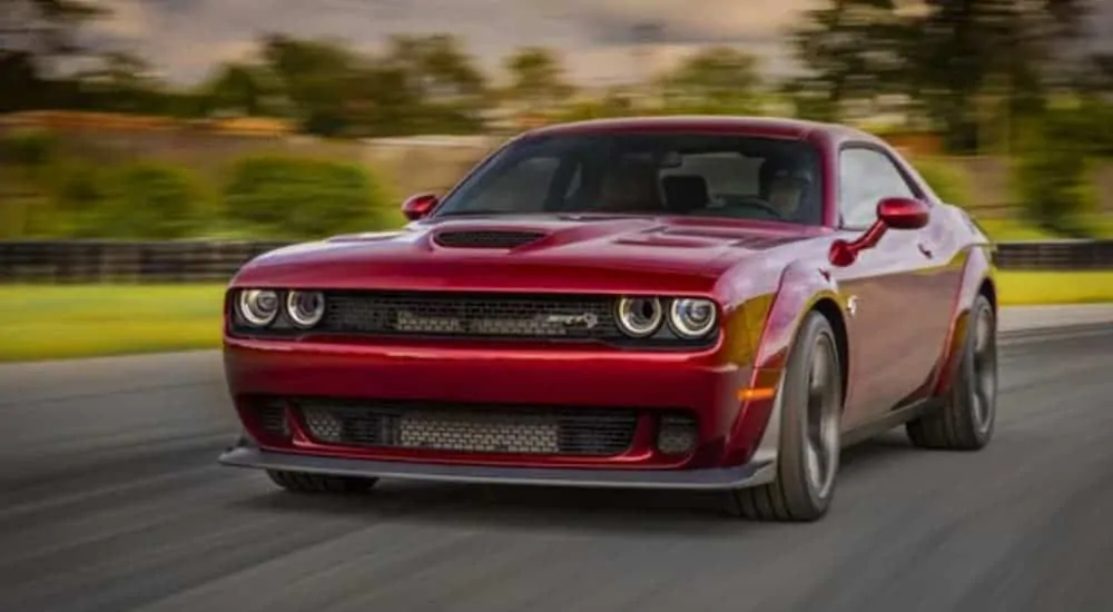 A red 2018 Dodge Challenger is driving on a racetrack past trees.
