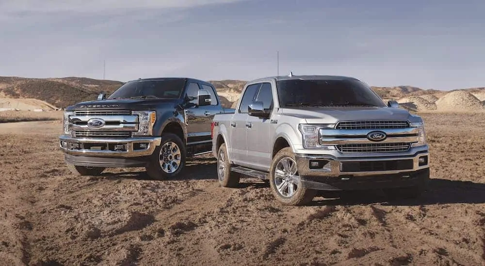 A 2018 Used Ford F-150 and F-150 are parked on dirt in front of distant hills.