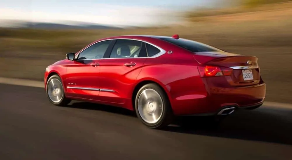 A red 2014 Chevy Impala is driving past blurred trees.