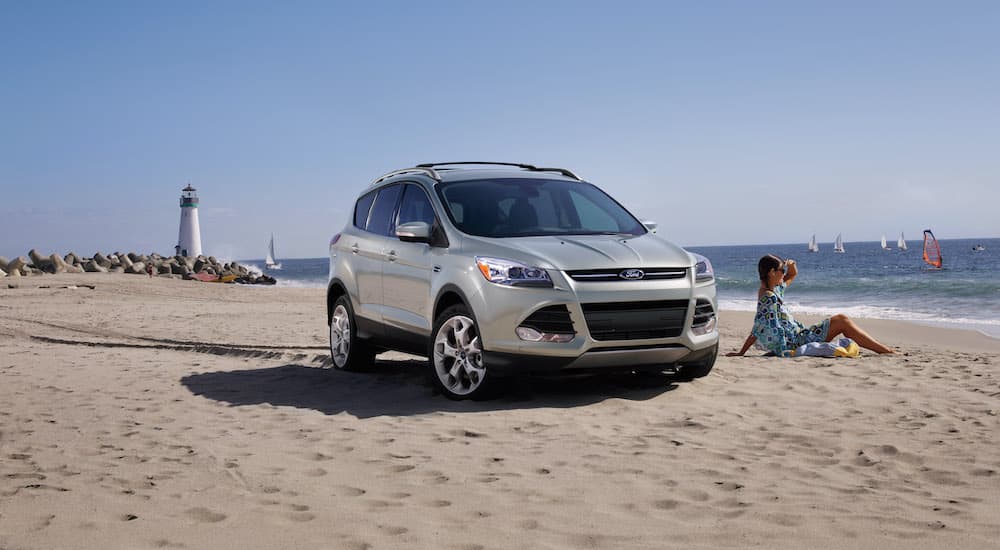 A silver 2013 used Ford Escape is parked on a sandy beach with a lighthouse in the distance.