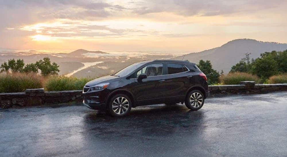 A black 2020 Buick Encore is parked on a mountain in front of a vibrant sunset and distant mountains.