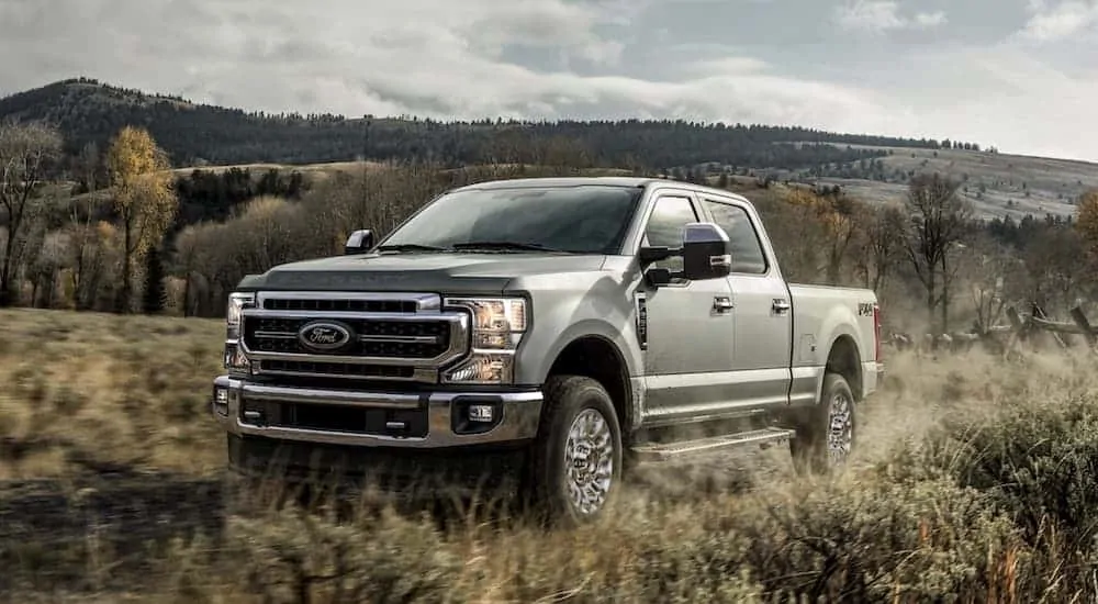 A silver 2020 Ford Superduty F-250 Lariat is driving through the grass after the 2020 Ford F-250 vs 2020 GMC Sierra 2500 comparison.