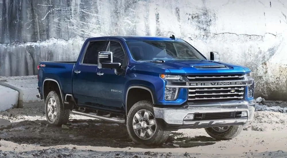 A blue 2020 Chevy Silverado 2500 is parked on sand in front of a cliff wall.