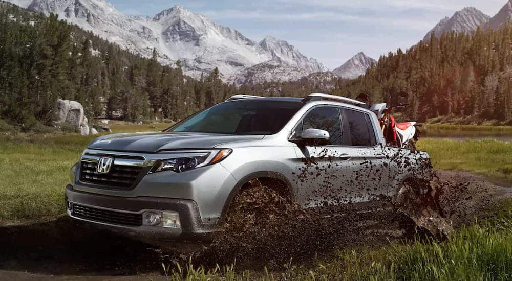 A silver 2020 Honda Ridgeline RTL-E is driving through the mud with a dirt bike in the bed.