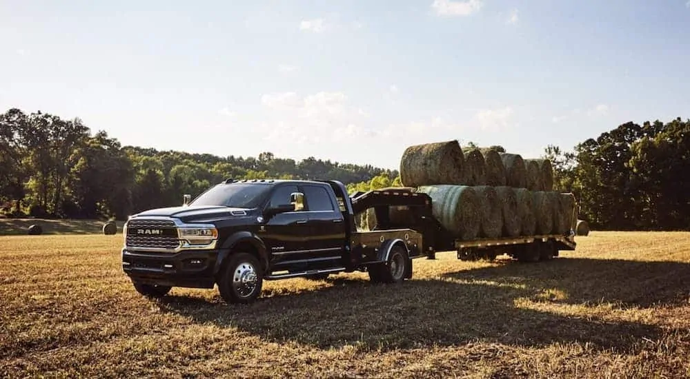 A black 2020 Ram 5500 is hauling bales of hay on a gooseneck trailer.