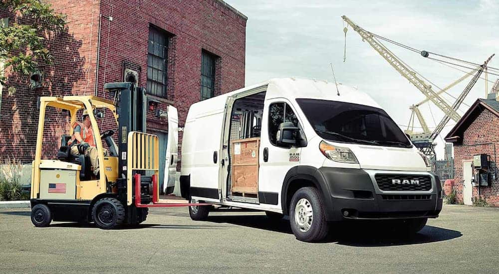 A white 2020 Ram ProMaster is having a crate loaded through its sliding door.