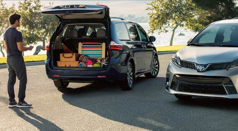 A man is loading cargo into the rear of a black 2020 Toyota Sienna which is parked next to a silver 2020 Toyota Sienna.
