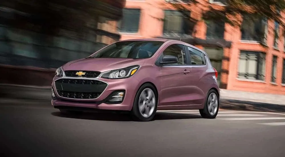 A magenta 2021 Chevy Spark is driving down a city street.