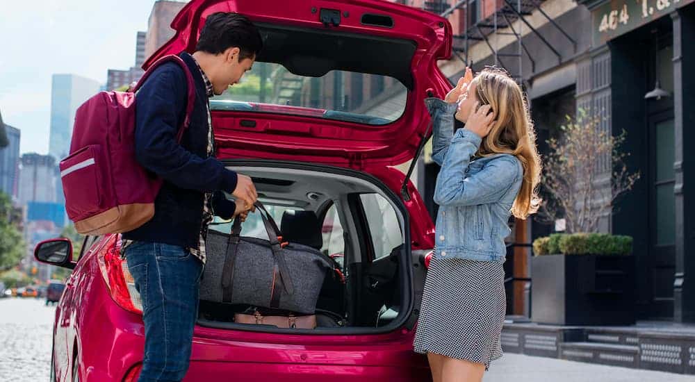 A red 2021 Chevy Spark is having luggage packed in the trunk by a man and woman.