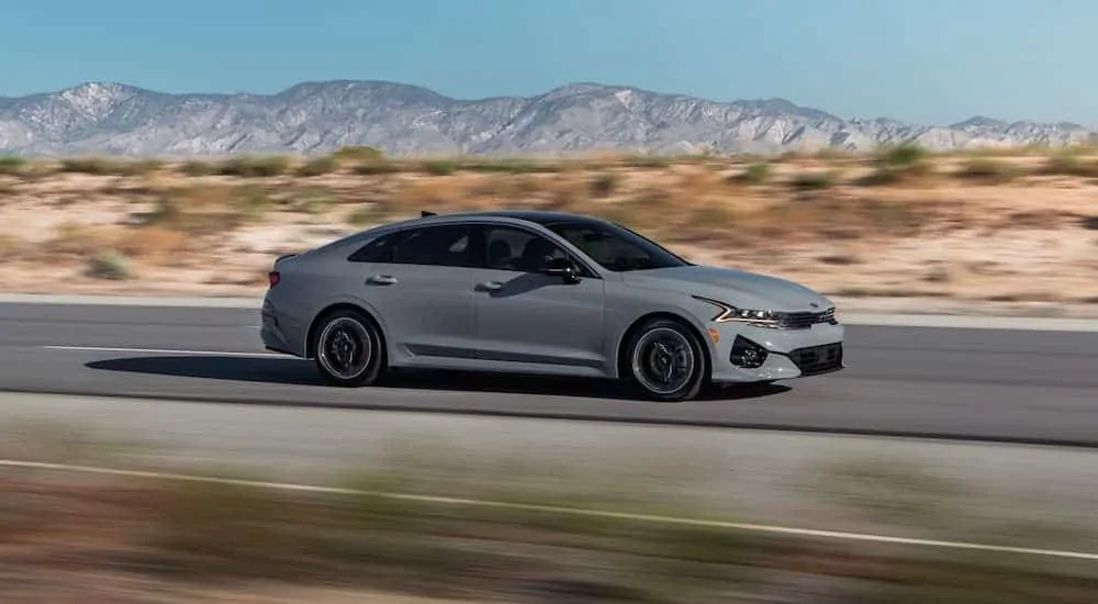 A grey 2021 KIA K5 GT is speeding down a desert road.