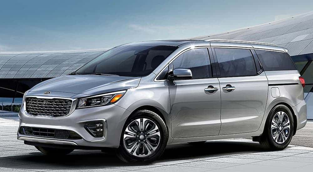 A silver 2021 Kia Sedona is parked in front of a rounded building.
