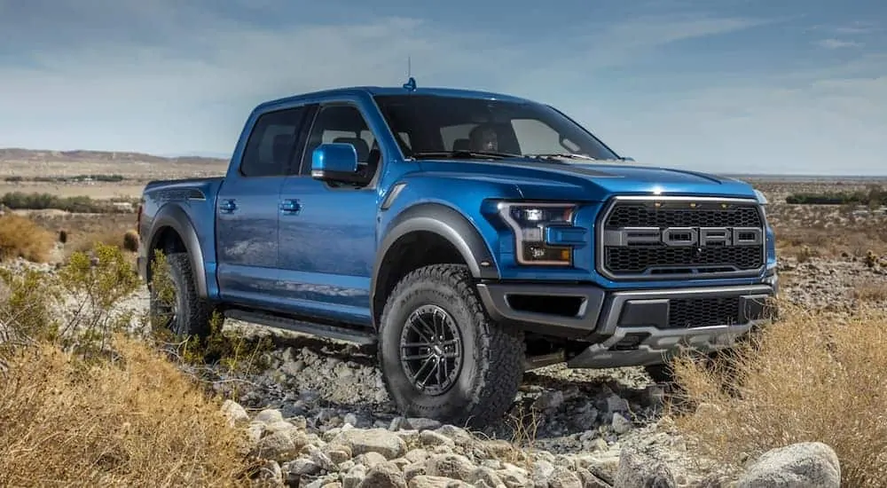 A blue 2020 Ford Raptor is parked off-road on a rocky trail.