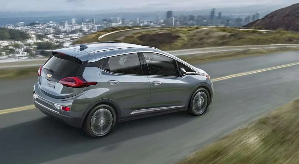 A silver 2020 Chevy Bolt EV, which is popular among cars for sale near me, is driving past a distant city.
