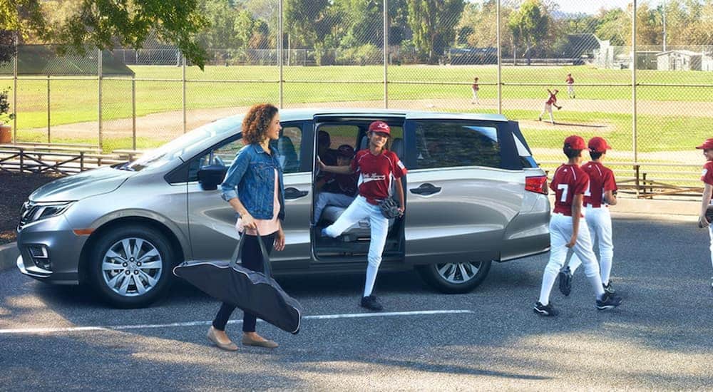 A woman and Little League team are getting out of a silver 2020 Honda Odyssey LX at a baseball field.