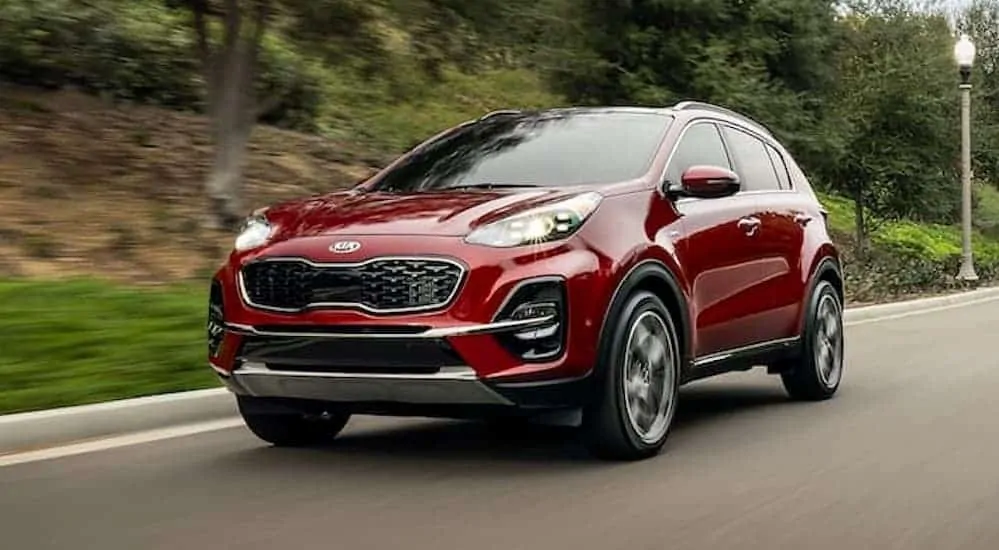 A red 2020 Kia Sportage is driving past grass and shrubs.