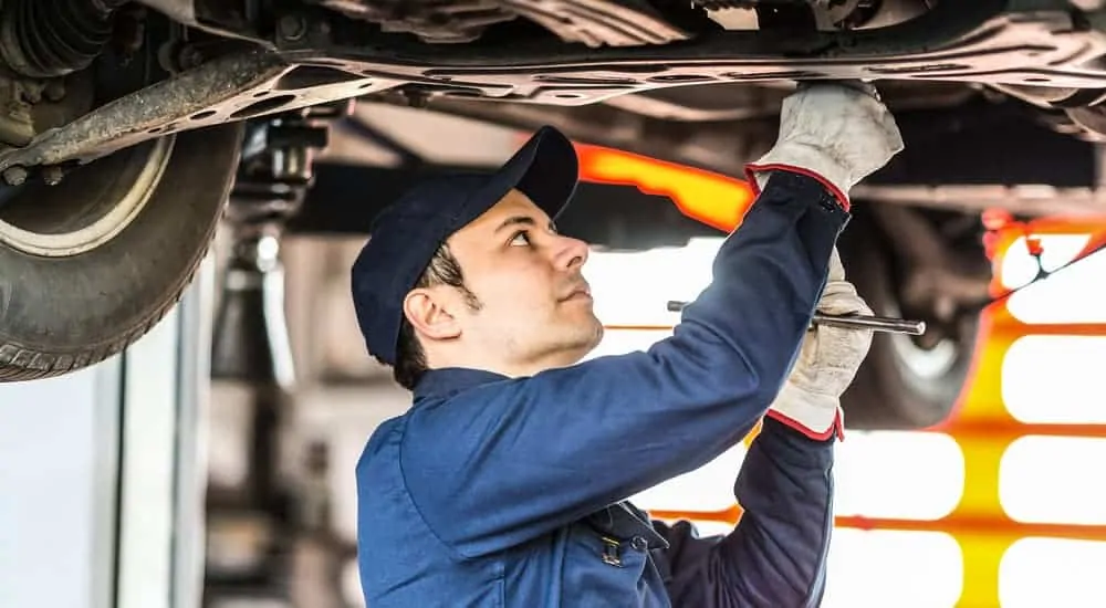 A mechanic is working under a car on a lift.