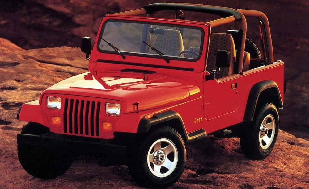 A red 1980s used Jeep Wrangler is parked on a desert cliff.