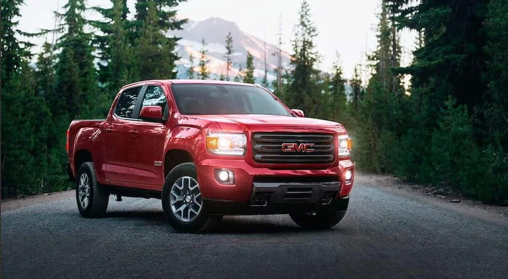 A red 2020 GMC Canyon All Terrain is parked near some evergreen trees after winning the 2020 GMC Canyon vs 2020 Toyota Tacoma comparison.