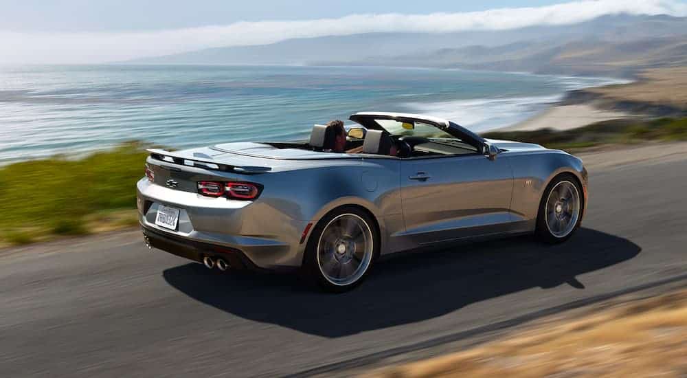 A grey 2021 Chevrolet Camaro convertible is driving down a road overlooking the ocean.