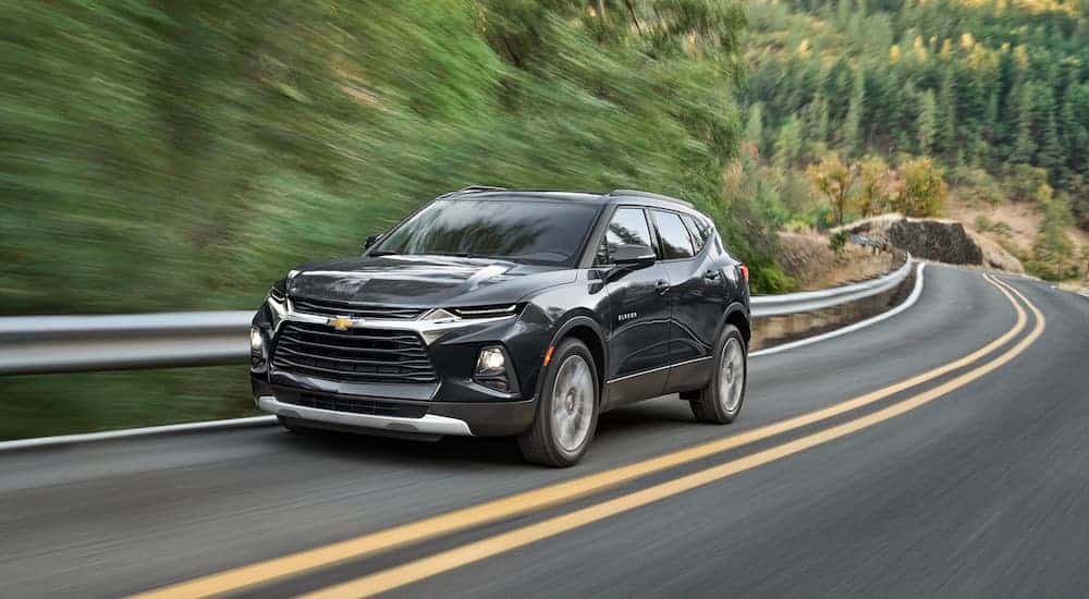 A black 2021 Chevy Blazer is driving down the highway passing trees.