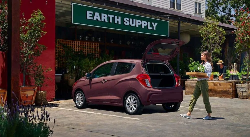 A magenta 2021 Chevy Spark is parked with the hatch open waiting for a woman to load in plants.