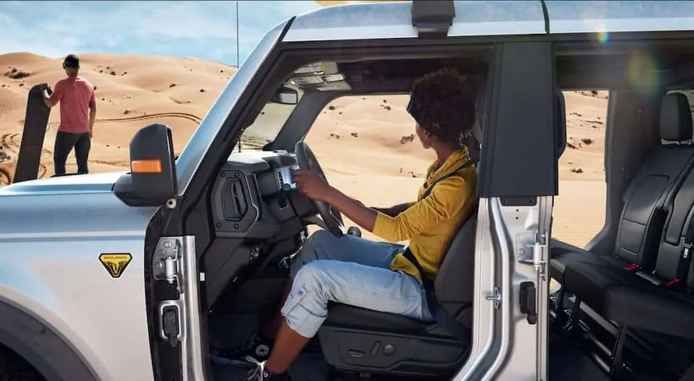 A silver Ford Bronco (4dr) Badlands is parked in the desert with its doors off.