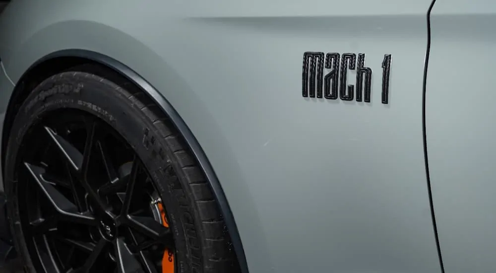 A close up is showing the badge of a white 2021 Ford Mustang Mach 1 with black rims.