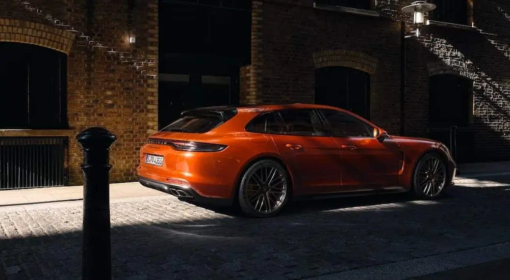 A orange 2021 Porsche Panamera is parked on a brick road partially in the shade.