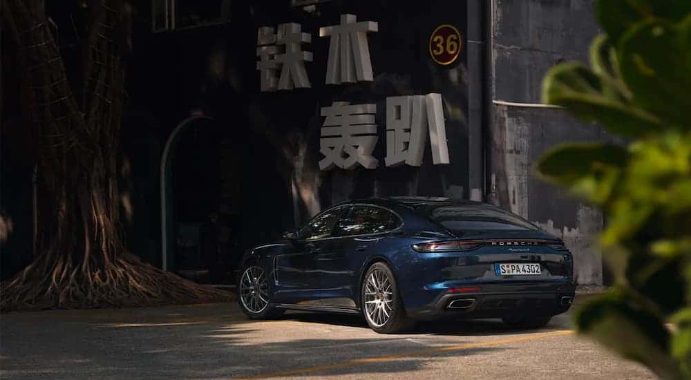 A blue 2021 Porsche Panamera is parked in front of a wall with large white kanji on it.